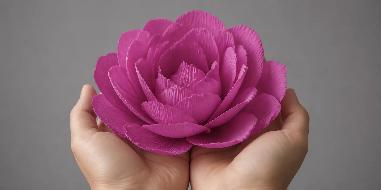 Manos sosteniendo una flor grande de papel crepé violeta rosáceo