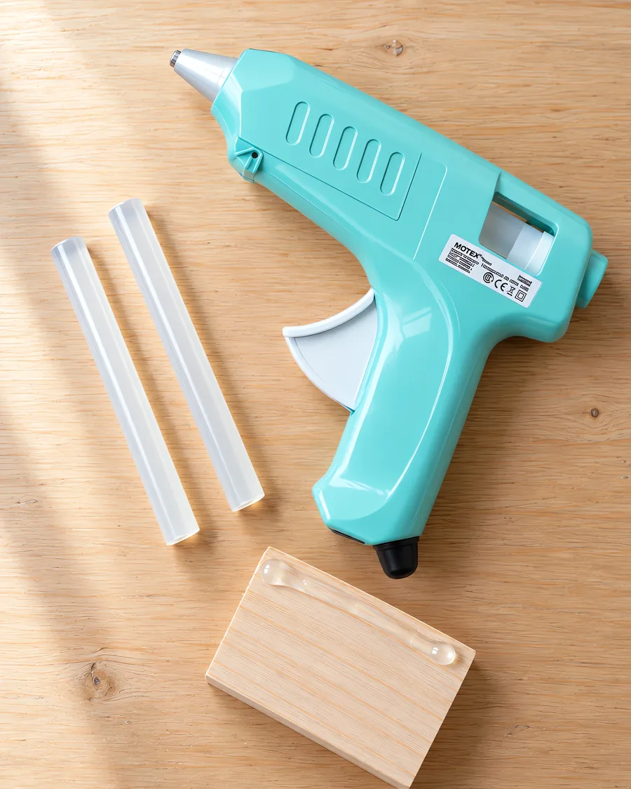Pistola encoladora verde agua de 72 W sobre la mesa, con dos barras de silicona al lado